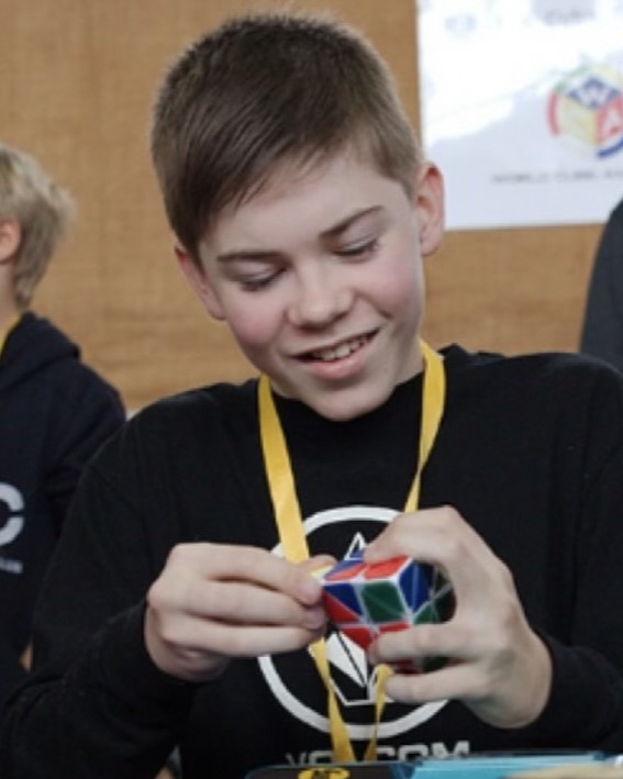 Dylan as a teenager, smiling as he solves a Pyraminx at a 2014 speedcubing competition